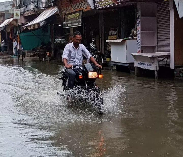 शामली के बड़ा बाजार में बारिश के बाद जलभराव के बीच से जाते बाइक सवार। संवाद शामली के बड़ा बाजार में बारिश के बाद जलभराव के बीच से जाते बाइक सवार। संवाद