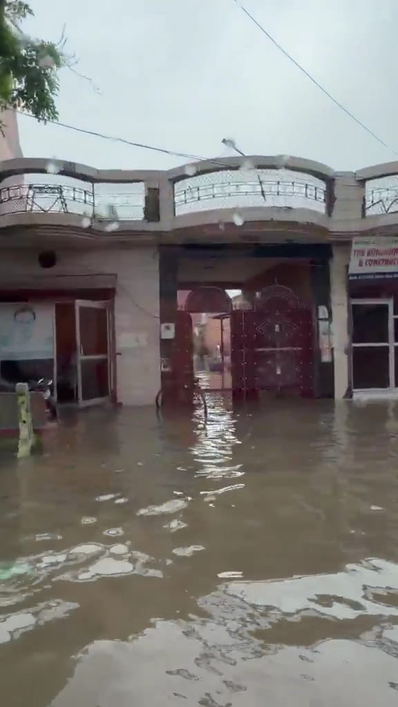 08jjrp25- शहर की एक कालोनी में घर में घुसे पानी को बाल्टी से निकालते परिवर के सदस्य। स्रोत : वी
