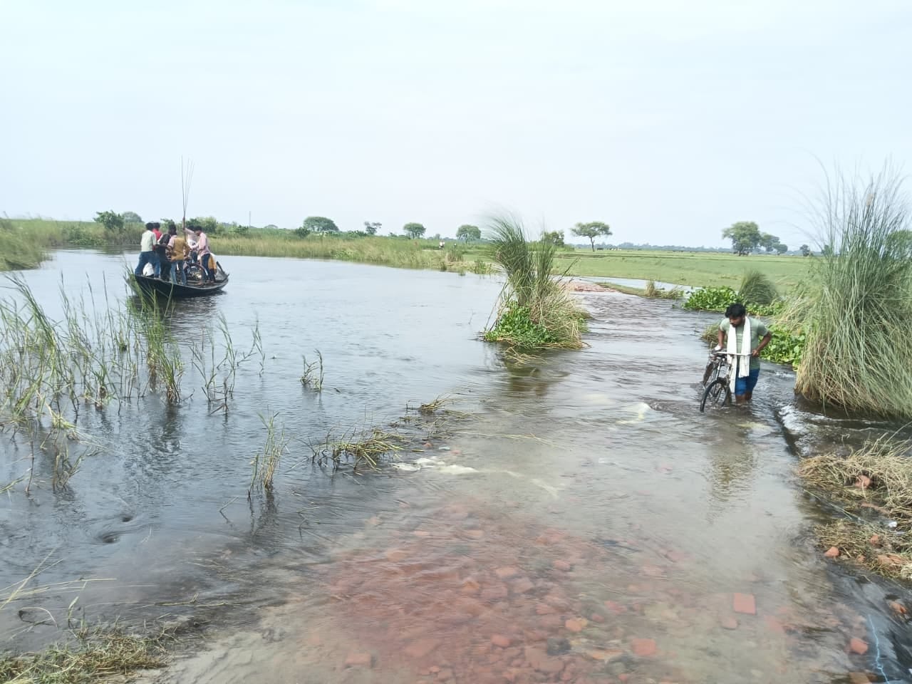 इस्माइलपुर में संपर्क मार्ग पर भरे पानी से बीच बोरे में सामान ले जाती महिला।