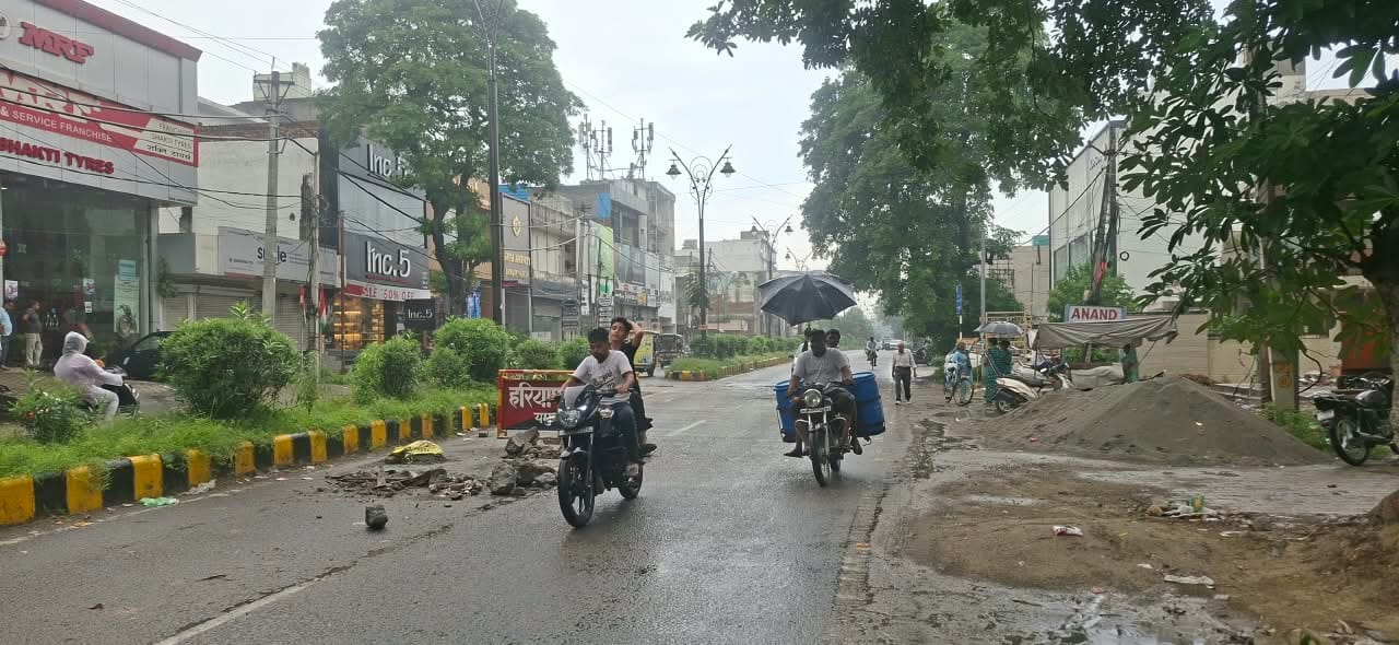 मॉडल टाउन में बारिश से बचने के लिए छतरी लेकर जाता व्यक्ति। संवाद
