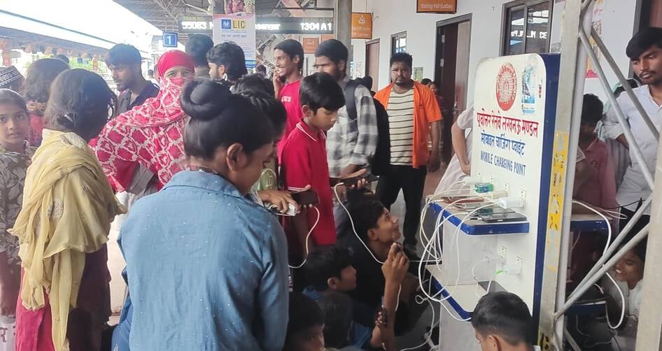 रेलवे स्टेशन पर जमीन पर एक्स्ट्रा बिजली का बोर्ड लगाकर बड़ी संख्या में एकत्र होकर मोबाइल चार्जि