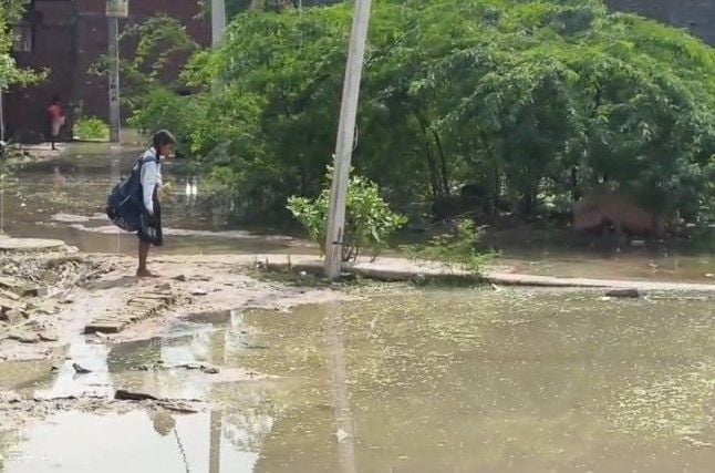 इंद्रानगर बजरंग चौराहे वाली गली में भरे पानी से निकलते लोग। संवाद