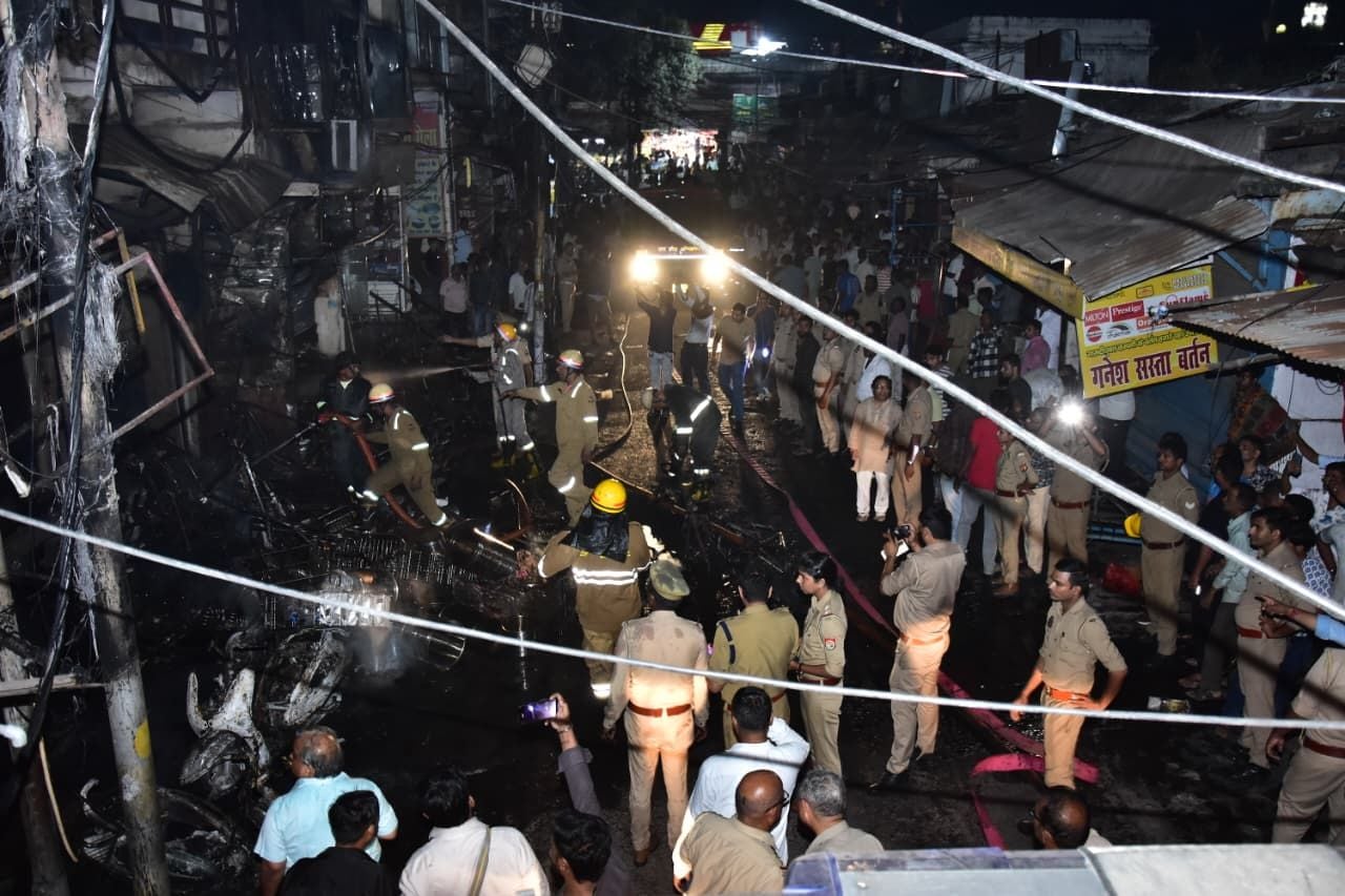 सदर बाजार स्थित ई स्कूटी शोरूम व बर्तन की दुकान से उठतीं लपटें व आग बुझाते दमकल कर्मी।