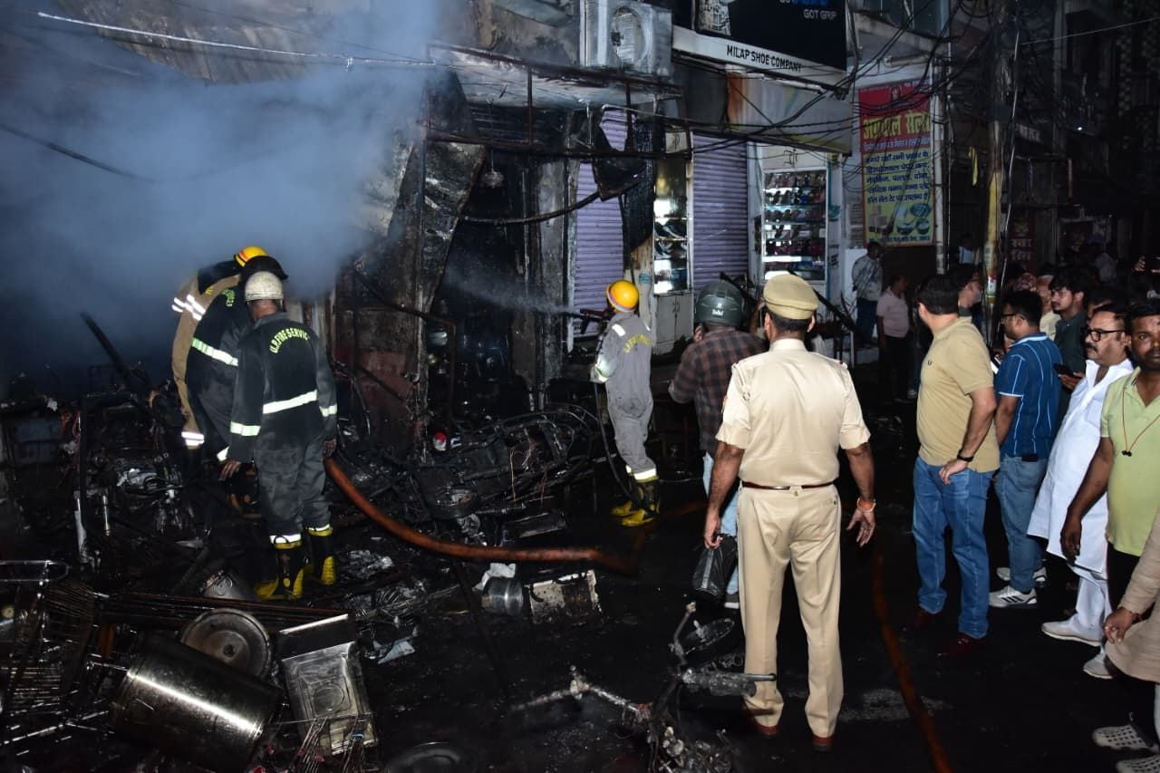 सदर बाजार स्थित ई स्कूटी शोरूम व बर्तन की दुकान से उठतीं लपटें व आग बुझाते दमकल कर्मी।