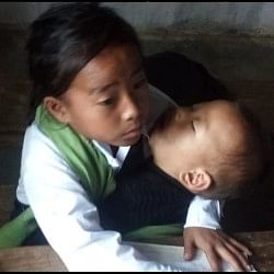 Girl reached the school to study with two year old younger sister in her lap